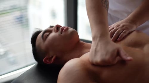 Closeup of Professional Male Chiropractor with Strong Tattooed Arms Massaging Pectoral Muscles of