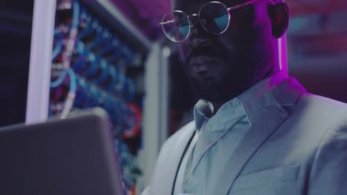 Man Works on Laptop in Server Room