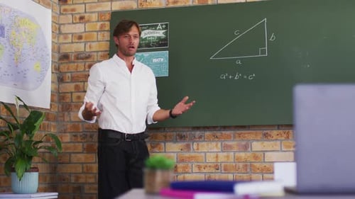 Caucasian male teacher teaching mathematics while looking at laptop in the classroom at school