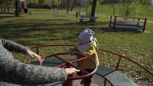Mother and son playing at merry-go-round in public playground, Zagreb, Croatia.
