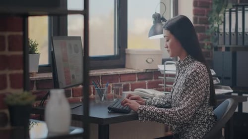 Woman Types at Computer in Urban Office
