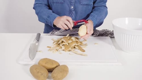 Person Peeling Potatoes on Cutting Board