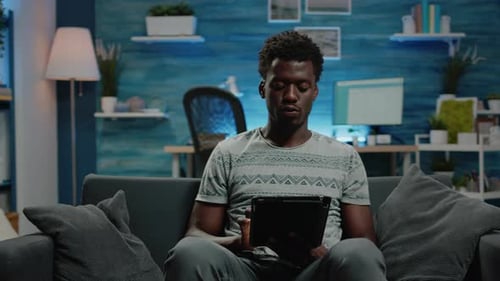 Young Adult Relaxing Using Tablet on Sofa Indoors