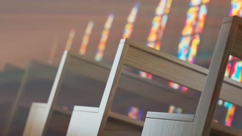 Endless rows of church benches lit by the sun through a stained glass window.