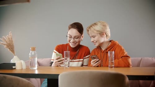 Two Friends Enjoying Smartphones Together at Table