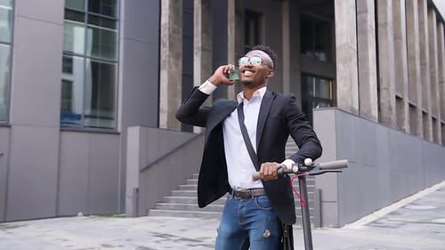 Black-Skinned Office Worker which Walking with His Own Electric Scooter and Talking on Phone