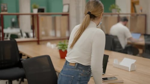 Une jeune entrepreneure dans un masque protecteur prend place dans son lieu de travail dans le bureau de coworking