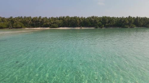 Flight of a drone over the Maldivian water towards the coast on which there are a lot of green trees
