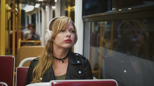 Female Hipster in Headphones is Riding a Tram Looking Out the Window and Listening to Music