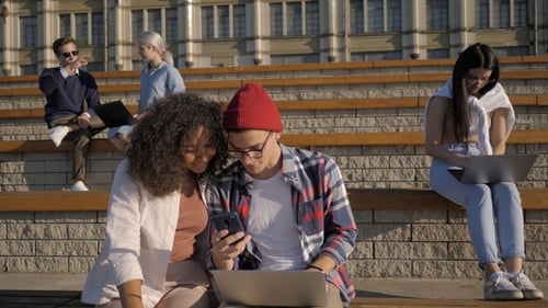 Beautiful couple uses the phone on a bench near college.