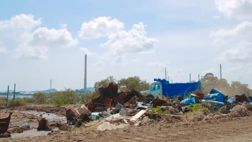 barrels with crude oil and water tanks lying on the ground with aing blue truck in the background