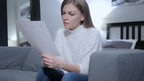 Worried Woman Reads Document on Gray Sofa