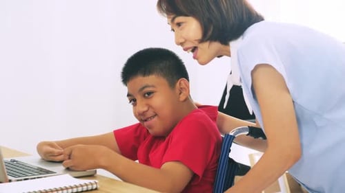Woman Helping Teen Boy in Wheelchair with Laptop