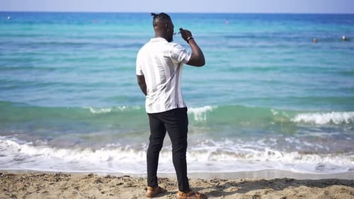 Back View Wide Shot of Handsome African American Bearded Man Standing on Sandy Beach Putting on