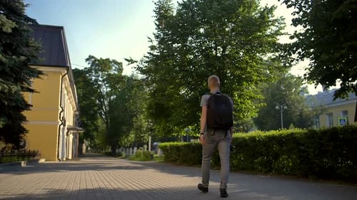 Young Photographer Is Walking Along a City Street Behind Him