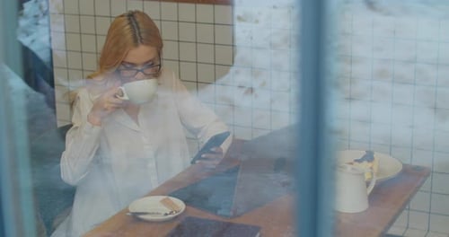 Female in Glasses Using App on Smartphone and Drink Tea in a Cafe