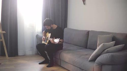 Retrato de un hombre con una guitarra en las manos en el sofá