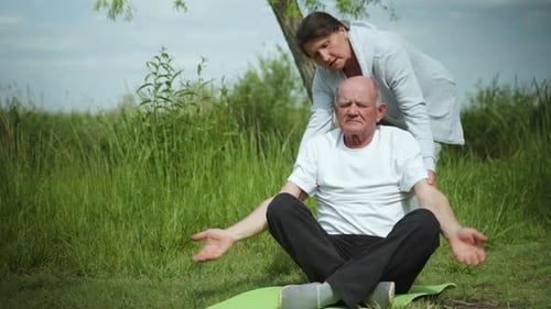 Woman Helping Senior Man Stretch Outdoors