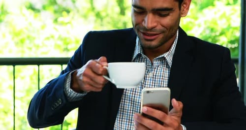 Young Adult Using Smartphone and Drinking Coffee Indoors