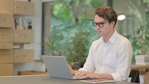Young Man Shaking Head As No Sign While Using Laptop in Modern Office