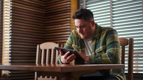 Man Sits at Table Using Tablet Device Indoors