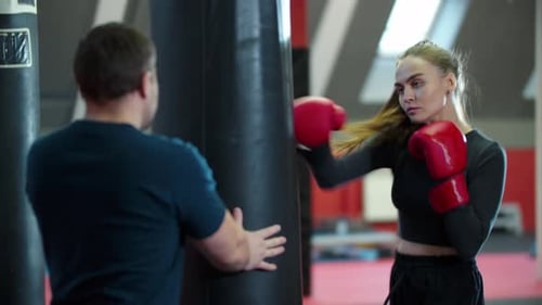 Boxing Training an Attractive Young Woman Punching the Bag and Her Coach Standing Behind It