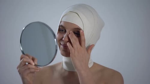 Woman With Bandages Looks at Herself in Mirror