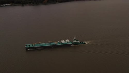 aerial shot over a turqiuse colored barge and tugboat on the Hudson River on a cloudy day in Beacon