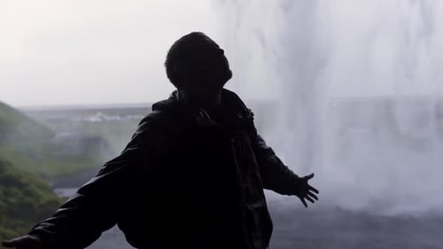 Traveler turning around under waterfall