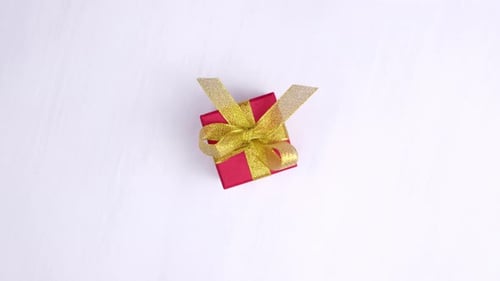Gift Box Red with Gold Ribbon Spinning on Pink Wood Background