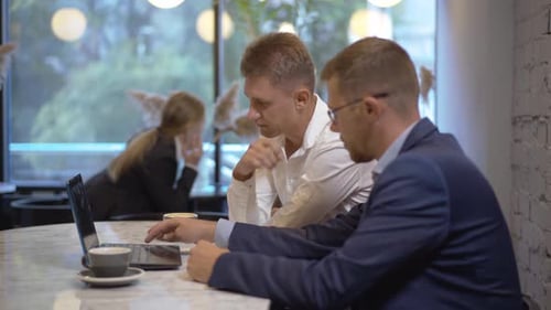 Busy Caucasian Businessmen Surfing Internet on Laptop at Lunch As Blurred Businesswoman Talking on