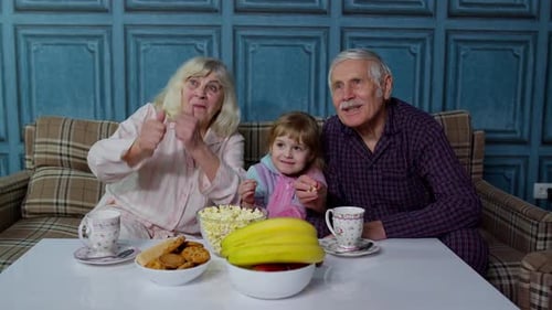 Grandparents Watch Television with Grandchild While Eating Popcorn