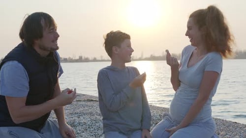 Slow Motion of Happy Parents with Crackers on the Coast at Sunset. Family Celebration.
