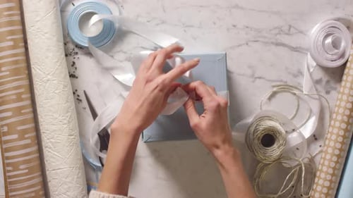 Tying White Ribbon on a Blue Gift Box