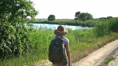 Woman Hiking with Backpack along Rural River Path