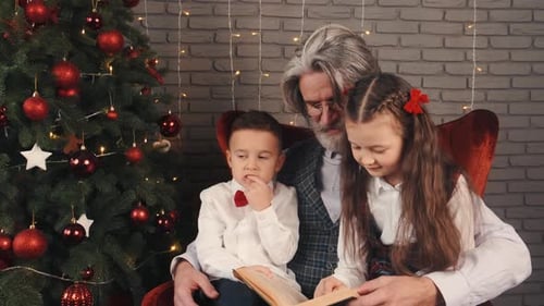 Grandfather Reading Book to Children near Christmas Tree