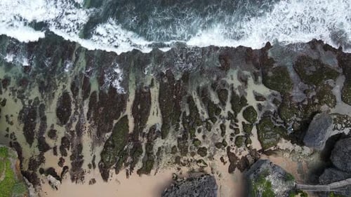 Top down aerial view of giant ocean waves crashing and foaming in coral beach