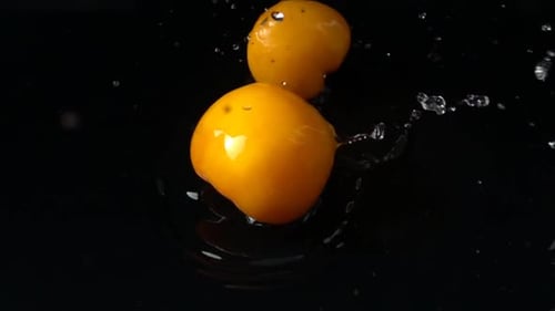 Two Yellow Tomatoes Dropping Into Water on Black