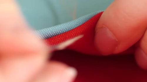 Woman`s Hands Sewing with Needle, White Thread and Thimble on Red and Blue Clothes, Close Up, Slow