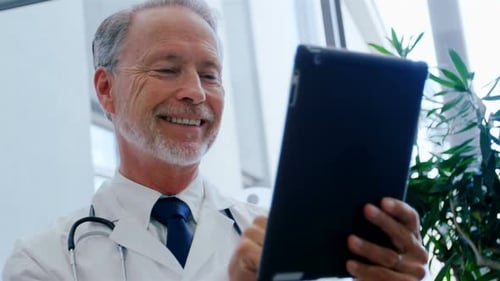 Caucasian male doktor working in a medical centre, wearing a lab coat and a stethoscope, using a tab