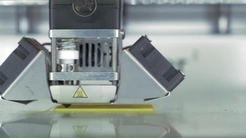 Vista frontal de cerca de la impresora 3D en proceso. Fabrica piezas para equipos con plástico amarillo
