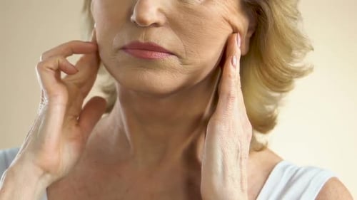 Woman Pulling Sagging Skin on Face With Fingers, Thinking About Plastic Surgery