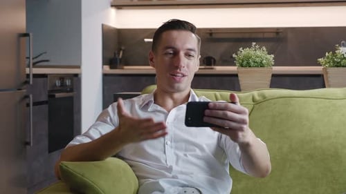 Enthusiastic man video calling from sofa at home