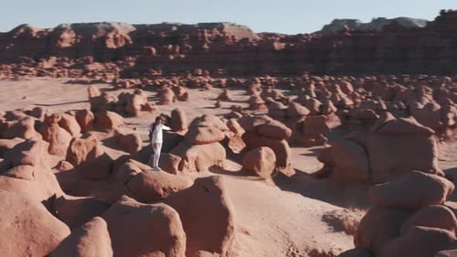 Young Woman with Backpack on Top of Red Rock Summit at Sunrise in Goblin Valley