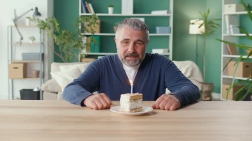 A Sad Elderly Man Celebrates His Birthday Alone at Home Blowing Out the Candle
