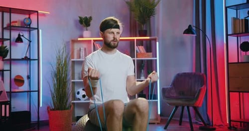 Cara em roupas esportivas sentado no Fitball e fazendo exercícios com expansor elástico
