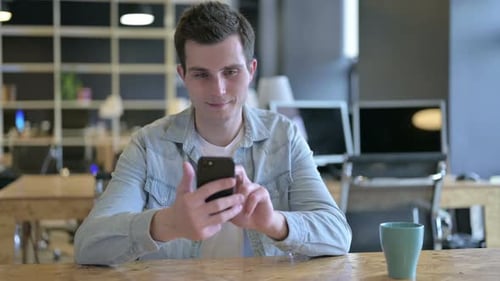 Attractive Young Designer Using Smartphone in Modern Office