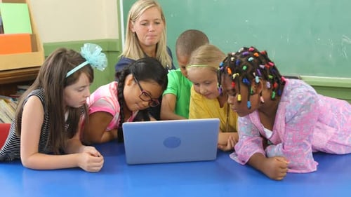 Teacher and students work on laptop computer in school classroom