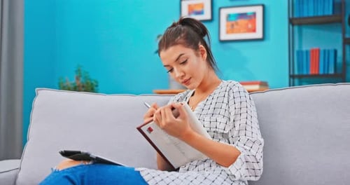 Young Woman Writing in Notebook on Sofa