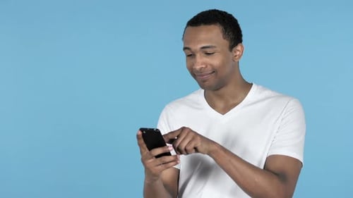 Young Adult Scrolling on Mobile Phone, Blue Background